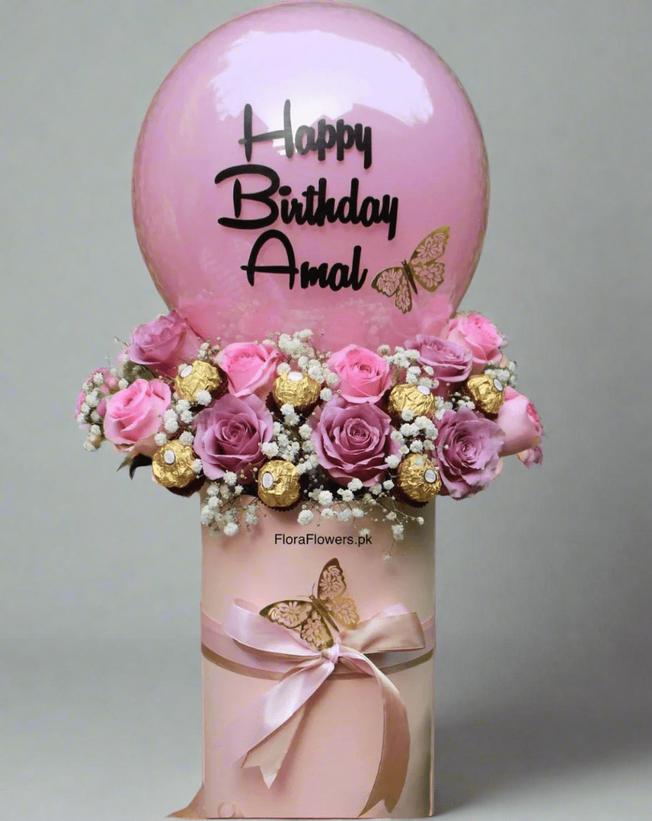 A birthday balloon with 'Happy Birthday Amal' printed on it, accompanied by an arrangement of pink roses, baby's breath, and chocolates.