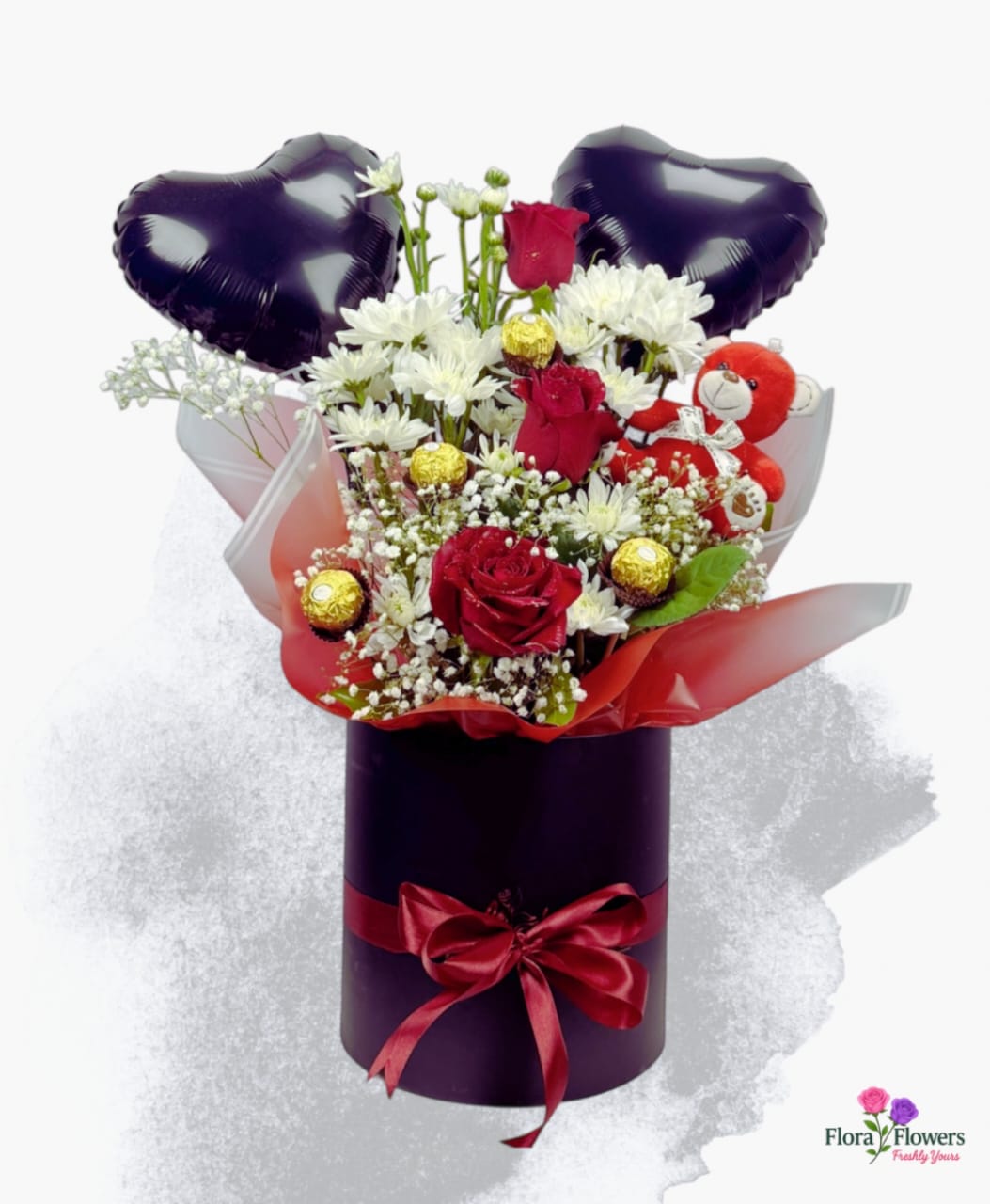 Floral arrangement with red roses, white flowers, and chocolate candies in a purple box with heart balloons on a white background.