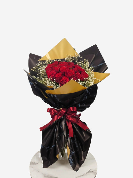 Bouquet of red roses wrapped in black paper with a gold leaf and red ribbon on a white background