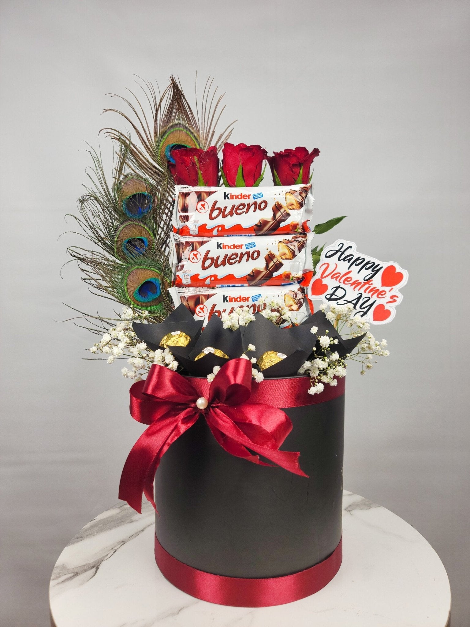 Valentine's Day gift basket with flowers, chocolates, and a peacock feather on a gray background