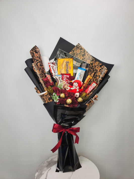 Bouquet of snacks and candies wrapped in black paper with a red bow on a white surface.