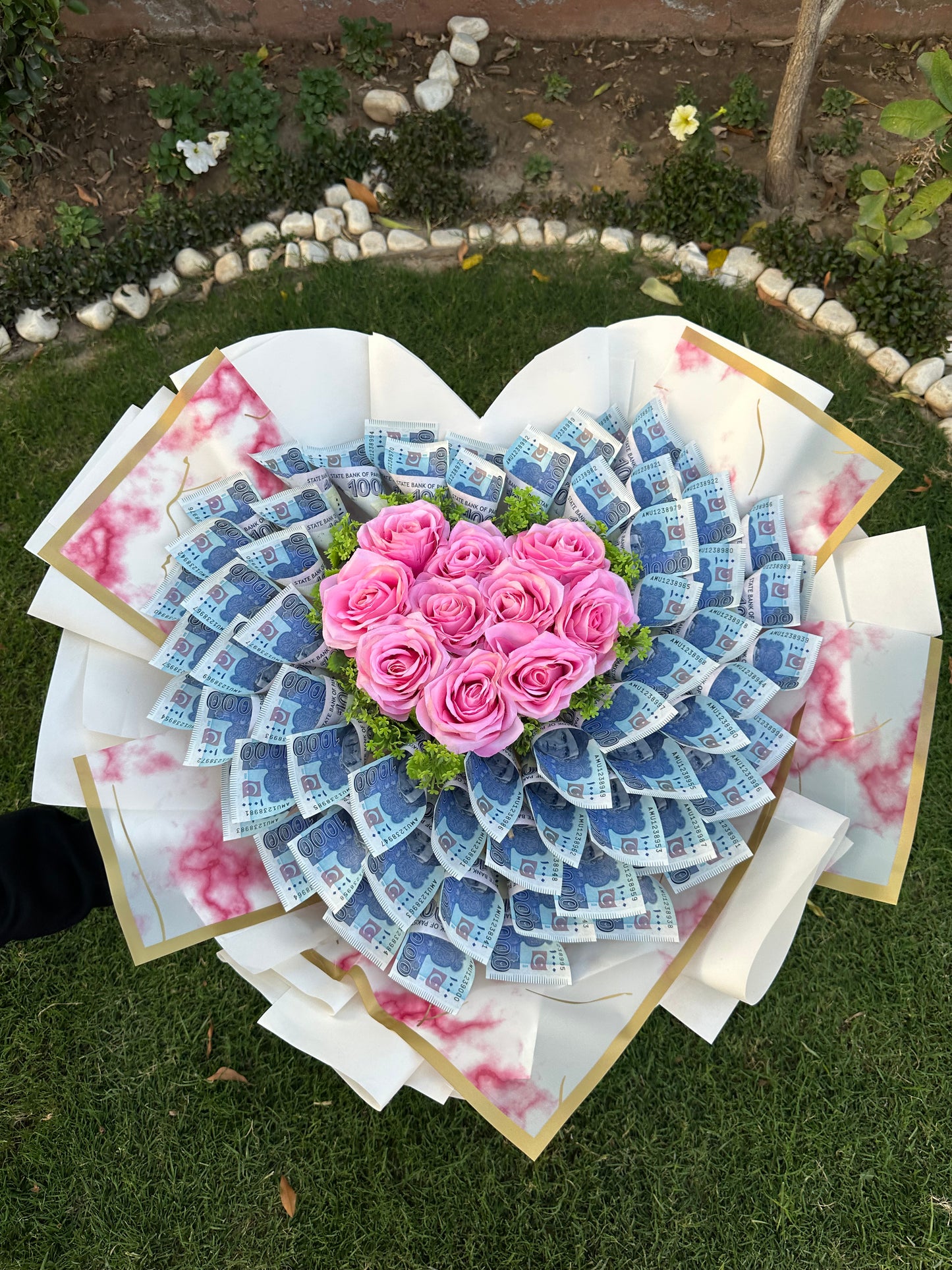 A bouquet of artificial roses arranged to form a heart, with the petals representing the leaves and the rose centers representing the flowers, laid on a grassy surface.