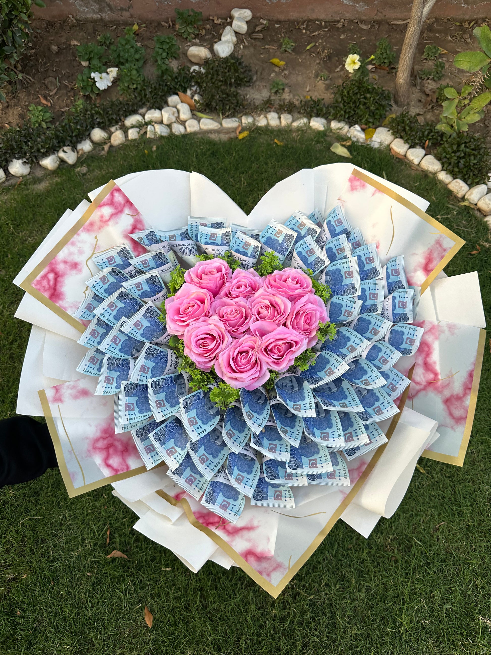A bouquet of artificial roses arranged to form a heart, with the petals representing the leaves and the rose centers representing the flowers, laid on a grassy surface.