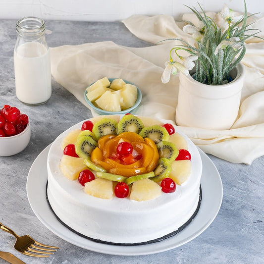 Fruit-topped cake on a gray surface with a bottle of milk, bowl of cherries, and plant in the background.