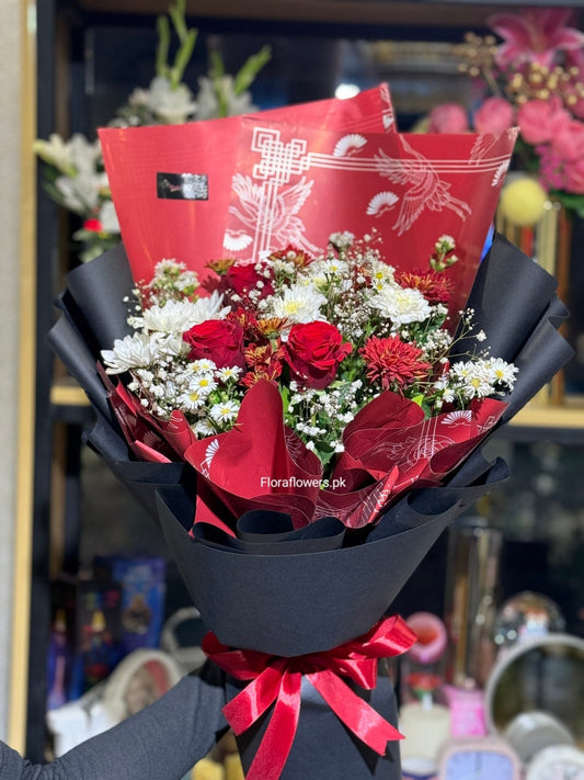 Bouquet of red and white flowers wrapped in black paper with a red ribbon, branded 'FloraFlowers.pk'.