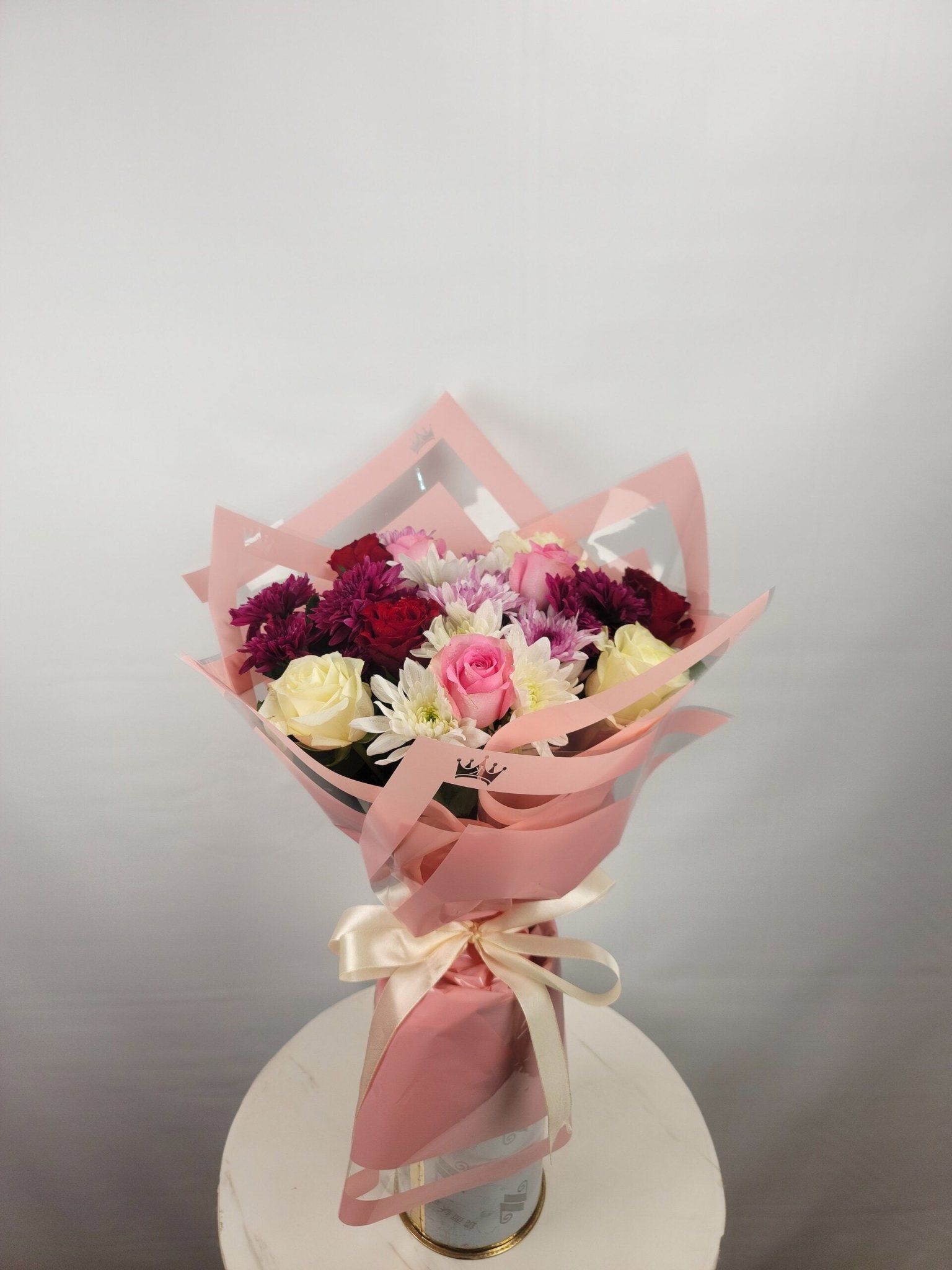 Bouquet of flowers wrapped in pink paper with a bow on a white surface.