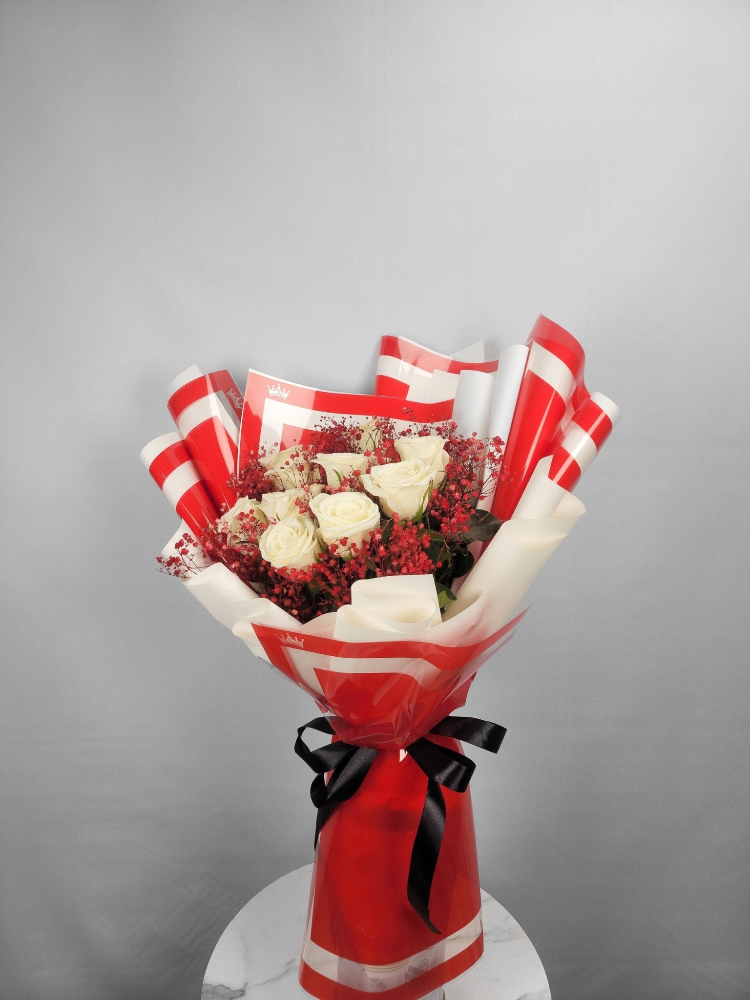 Bouquet of flowers wrapped in red and white paper with a black bow on a gray background