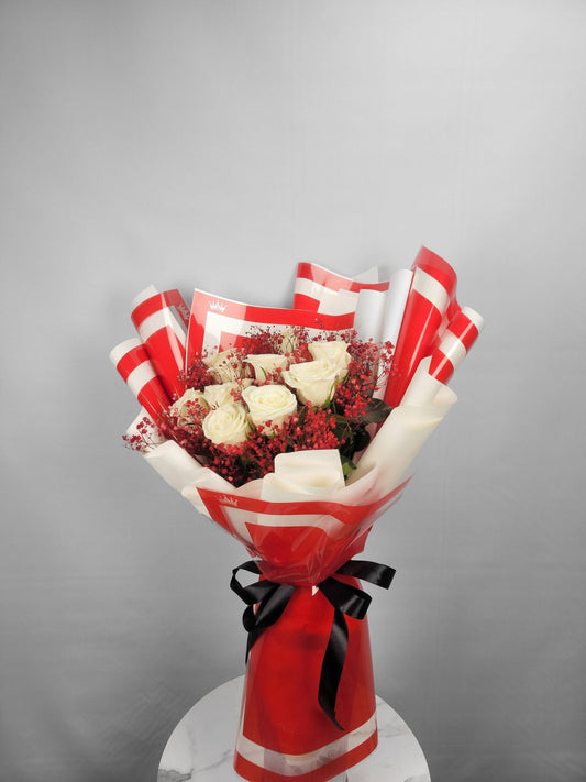Bouquet of flowers wrapped in red and white paper with a black bow on a gray background
